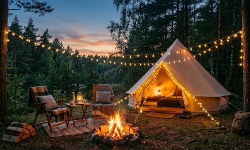 A cozy lit tent and camping chairs set up at dusk.